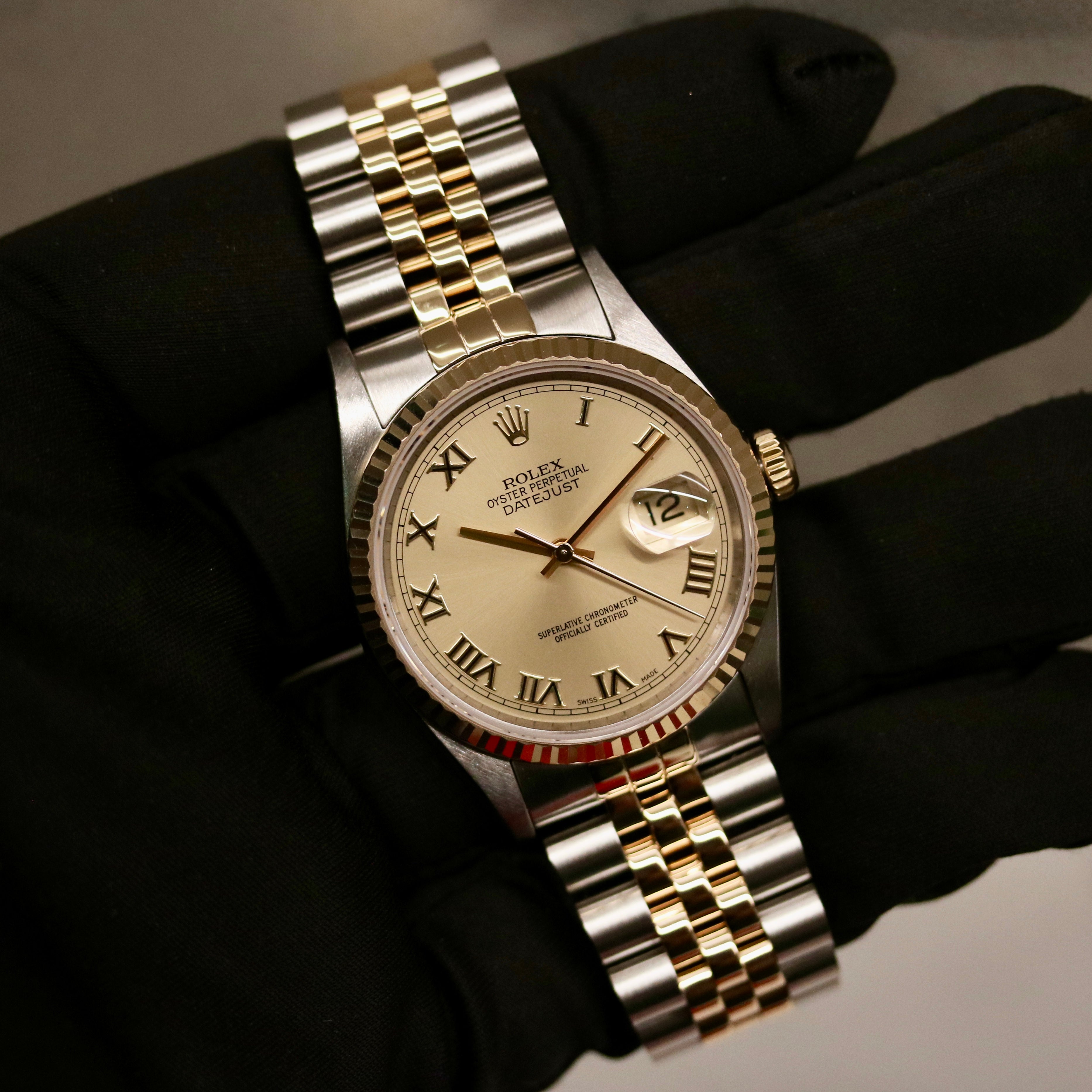 Rolex Datejust 36 ref. 16233 from 2003 in two-tone steel and yellow gold with a champagne Roman numeral dial, 36mm case, Jubilee bracelet, sapphire crystal, and automatic movement. Detailed product photos showing the fluted yellow-gold bezel, Roman hour markers, bracelet links, clasp, and overall condition. Includes original Hong Kong 2003 certificate, box, and tag, offered by Klocksalongen with a 12-month functional warranty.