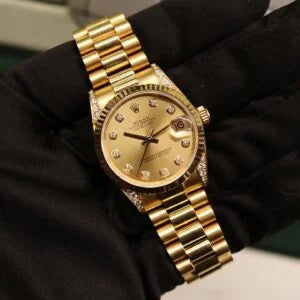 Rolex Datejust 31 ref. 68238 from 2000 in solid yellow gold with factory diamond-set bezel and a factory champagne big diamond dial, 31mm case, President bracelet, sapphire crystal, and automatic movement. Excellent condition, freshly serviced, and complete with original 2000 Spain certificate, box, booklets, and tag. Detailed product photos showing the diamond bezel, large diamond markers, gold case, bracelet, clasp, and finishing, offered by Klocksalongen with a 12-month service warranty.