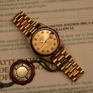 Rolex Datejust 31 ref. 68238 from 2000 in solid yellow gold with factory diamond-set bezel and a factory champagne big diamond dial, 31mm case, President bracelet, sapphire crystal, and automatic movement. Excellent condition, freshly serviced, and complete with original 2000 Spain certificate, box, booklets, and tag. Detailed product photos showing the diamond bezel, large diamond markers, gold case, bracelet, clasp, and finishing, offered by Klocksalongen with a 12-month service warranty.