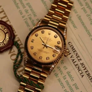 Rolex Datejust 31 ref. 68238 from 2000 in solid yellow gold with factory diamond-set bezel and a factory champagne big diamond dial, 31mm case, President bracelet, sapphire crystal, and automatic movement. Excellent condition, freshly serviced, and complete with original 2000 Spain certificate, box, booklets, and tag. Detailed product photos showing the diamond bezel, large diamond markers, gold case, bracelet, clasp, and finishing, offered by Klocksalongen with a 12-month service warranty.